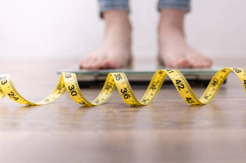 Person stands on weight scales with measuring tape in front. Weight Management Services available at Narangba Station Medical Centre.