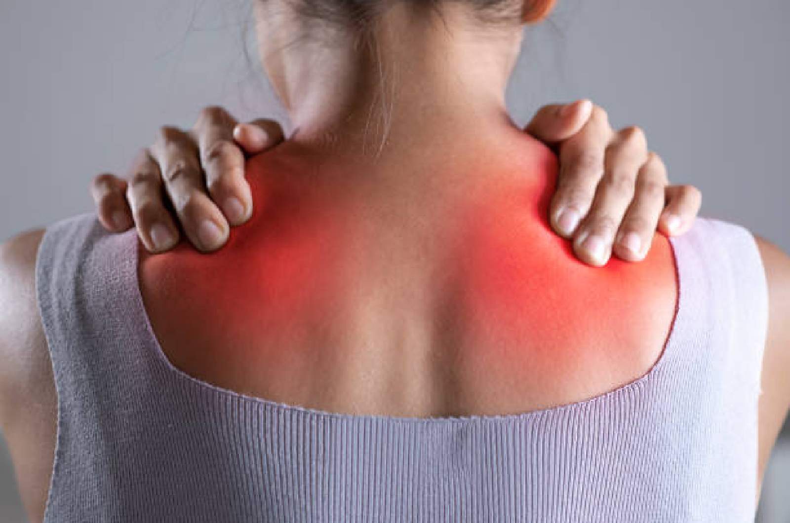 An individual holds their hands on their neck and shoulders as they experience pain caused by fibromyalgia