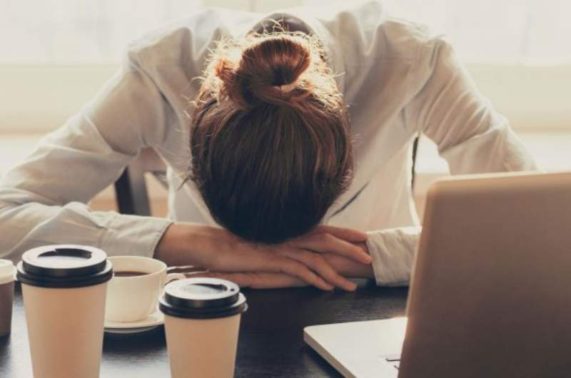 Individual suffering from chronic fatigue syndrome with head in hands on desk.