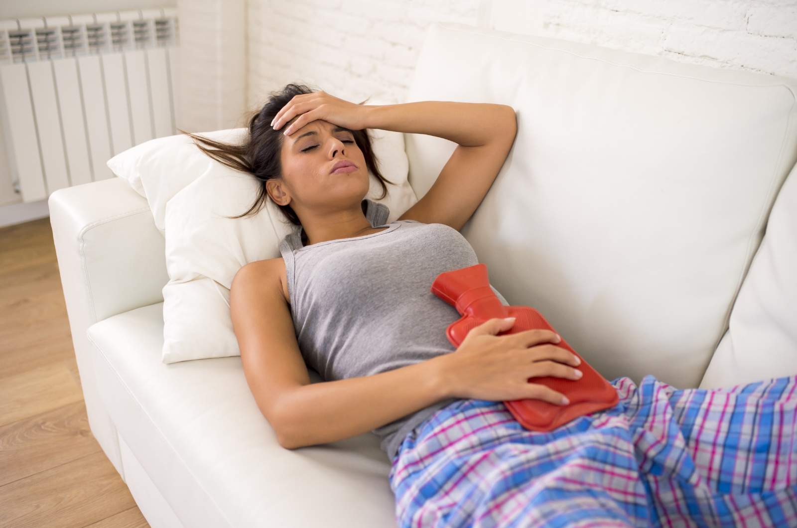 A woman lies on a couch with hot water bottle on stomach as she experiences pain caused by endometriosis.