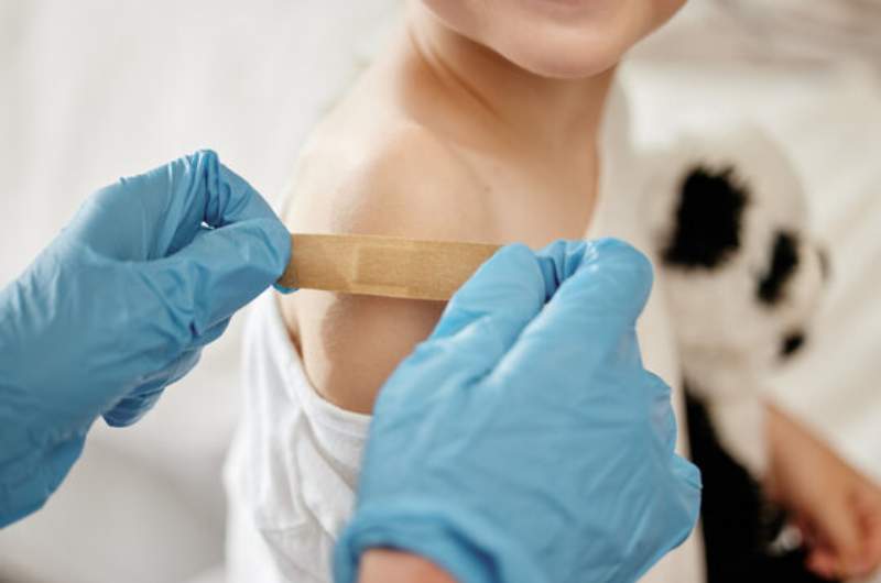 Child receives polio vaccination by nurse who places plaster over vaccination area while child holds panda toy.