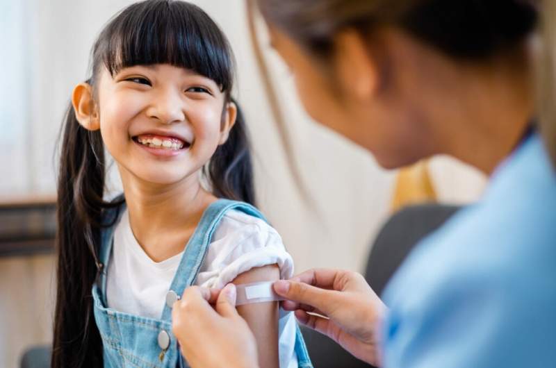 Child receiving rabies vaccination with nurse placing plaster over arm and child smiling.