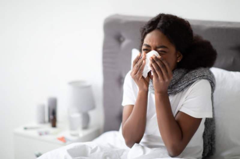 Woman sitting in bed ill with typhoid fever wiping nose with tissues.