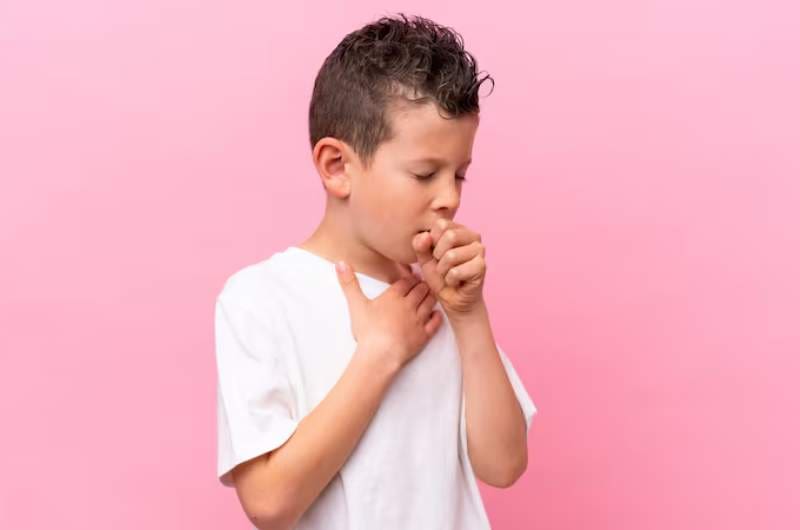 Young boy with his hand to mouth covering cough while holding his chest with his other hand.