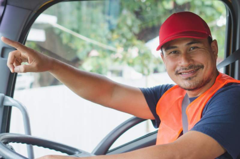 A young male commercial driver sits in the driving seat of a commercial truck smiling after having a Commercial Driver Assessment at Narangba Station Medical Centre.